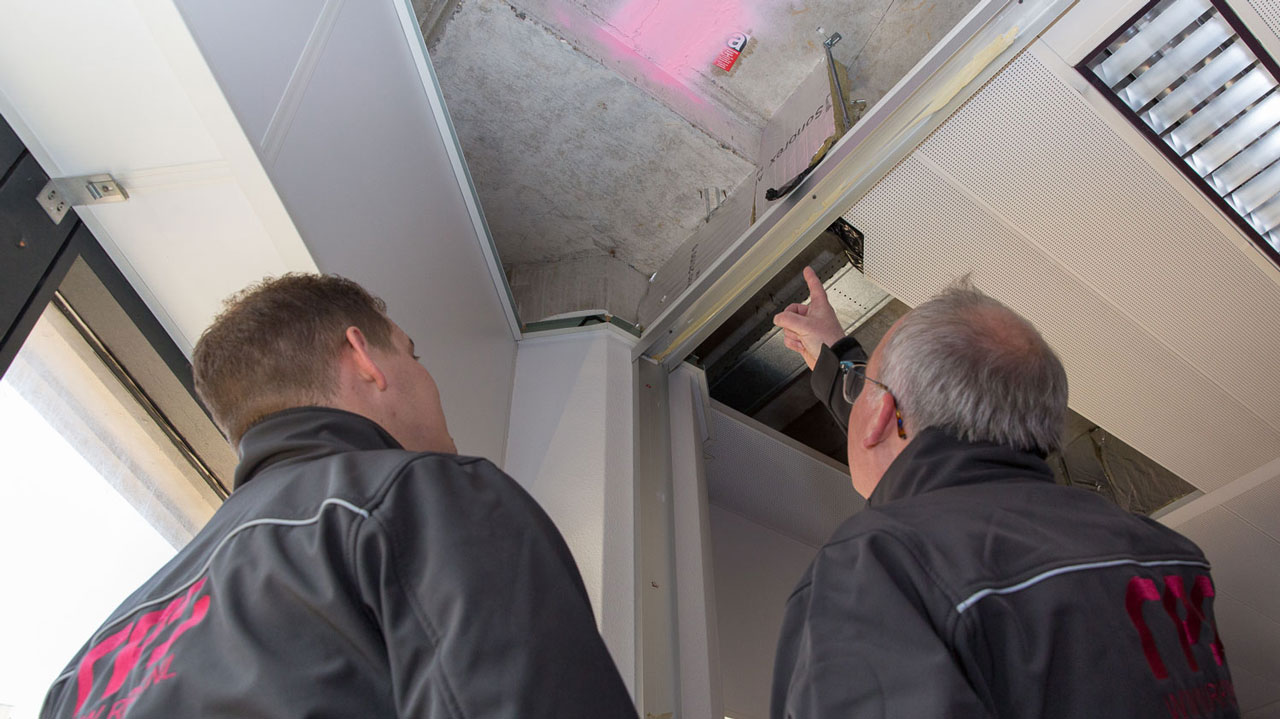 Inspectie plafond Hoog Catharijne Utrecht tijdens asbestinventarisatie, met twee specialisten in werkkleding bij open plafondpaneel