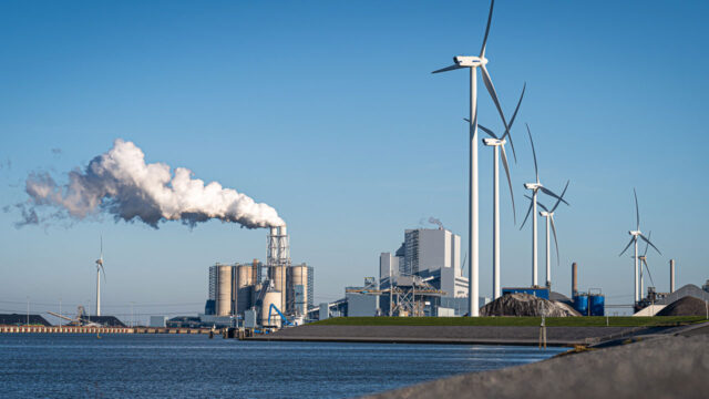 Industrieterrein met windturbines en fabriek bij water, illustratie van werkomgeving waar biomonitoring bijdraagt aan veiligheid en gezondheid