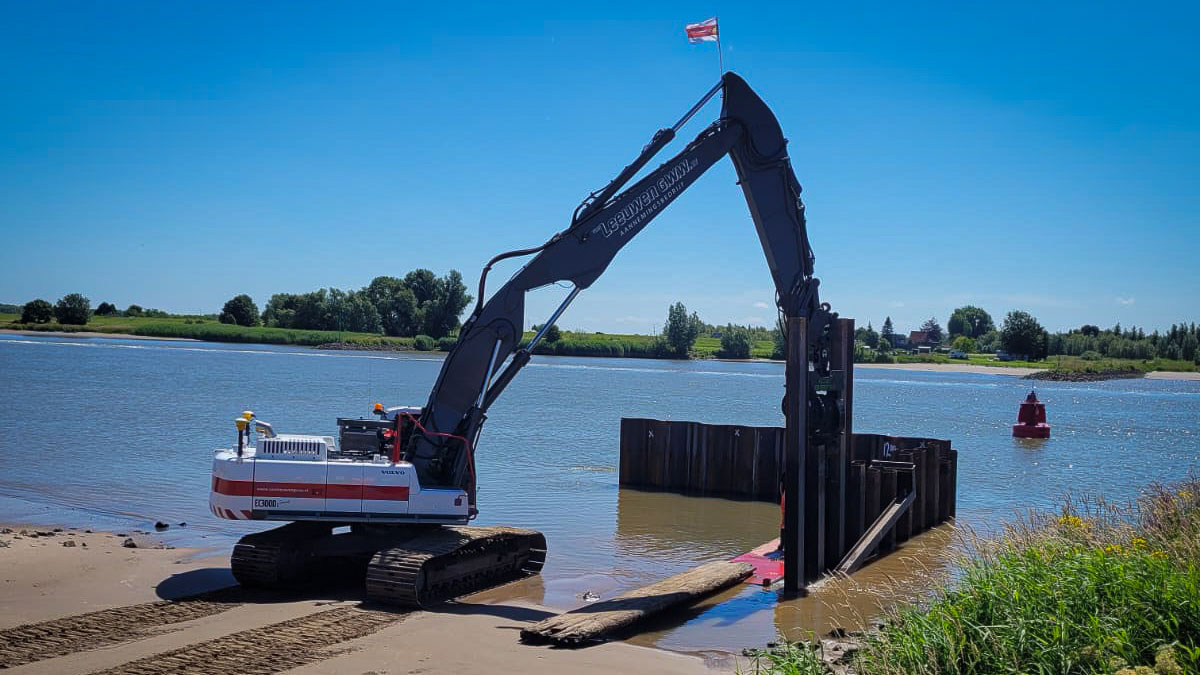 Graafmachine plaatst houten beschoeiing bij dijkversterking Salmsteke langs rivier, met damwand en groene oeverzone