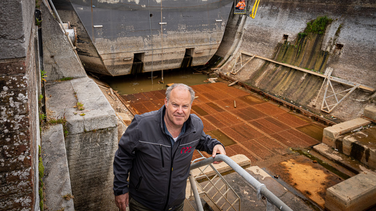 Man bij lege droogdok met zicht op droogdokdeuren en werkzaamheden, illustratie van maritieme inspectie in havenomgeving