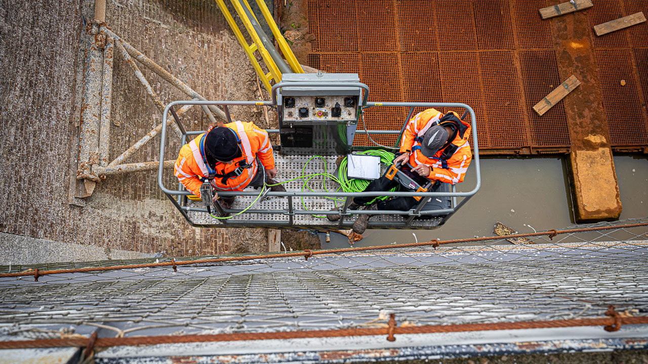 Medewerkers op hangplatform inspecteren verticale structuur in droogdok, onderdeel van maritiem onderhoud en veiligheid