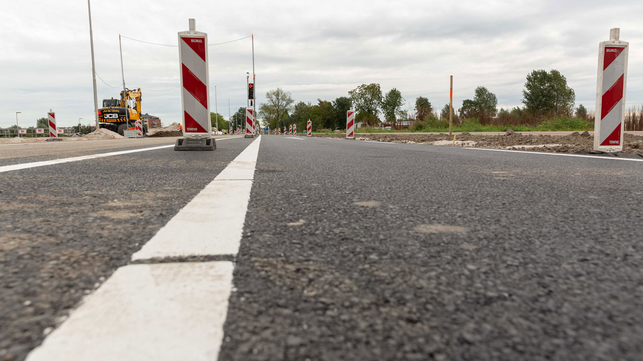 Nieuw aangelegde weg Vredenburghlaan met verkeersbarrières en graafmachine, onderdeel van duurzame aanbesteding
