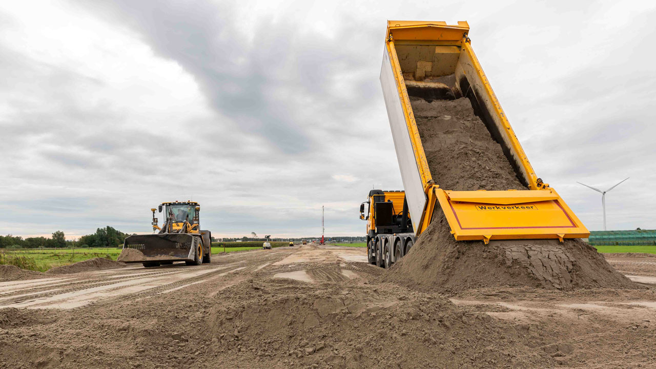 Bouwplaats Vredenburghlaan met vrachtwagen, bulldozer en windmolens, onderdeel van duurzame aanbesteding