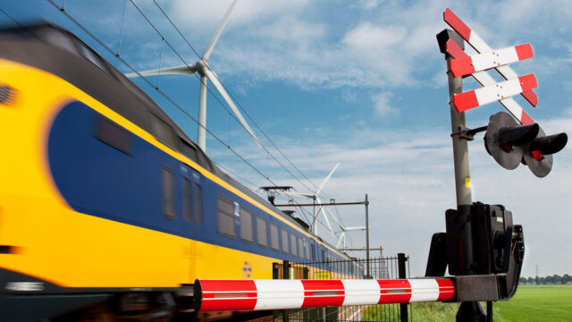 Trein passeert spoorwegovergang met windmolens op achtergrond, symbool voor digitalisering en vernieuwing van spoorinfrastructuur door GRIP