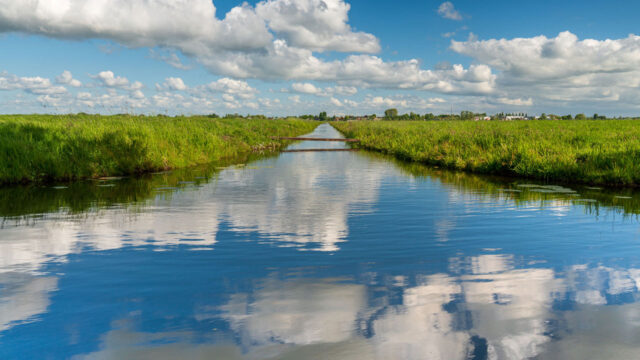 Kanaal met groene oevers en brug in polderlandschap, onderdeel van pragmatische toetsing van polderkaden door Tetra Tech