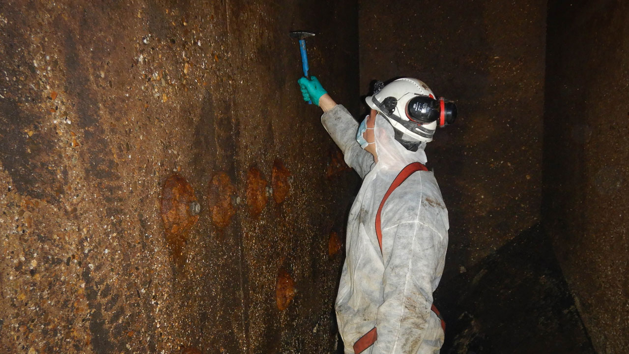 Met een hamer kloppen op de tankwand in beschermende kleding – specialistisch werk binnen inspectie van Utrechts rioolgemaal