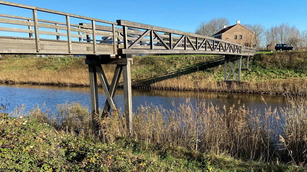 Houten voetbrug over uitwateringskanaal Zeeuws-Vlaanderen met rietoevers