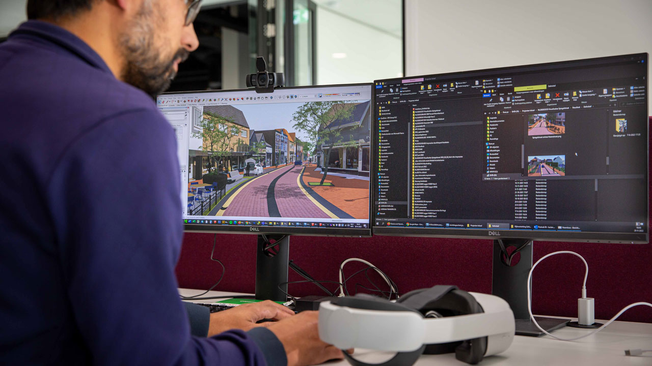 Medewerker ontwikkelt virtuele omgeving voor bewonersparticipatie met VR bij stedelijke projecten, zichtbaar op dubbele monitor en VR-headset