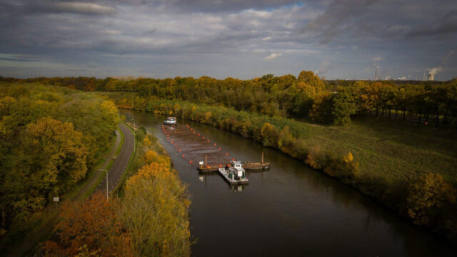 Vrachtschip op Julianakanaal tussen herfstbomen, met parallelle weg en sleepboot, onderdeel van verruimingsproject vaarweg