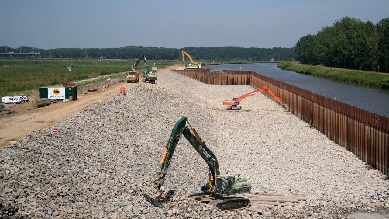 Bouwplaats langs Julianakanaal met graafmachines en damwand, waar verruiming vaarweg voor vrachtschepen plaatsvindt