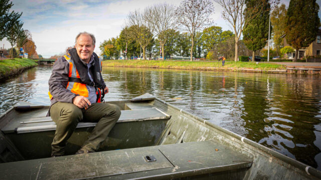 Medewerker inspecteert watergang per boot in woonwijk, onderdeel van grootschalig beheer en onderhoud