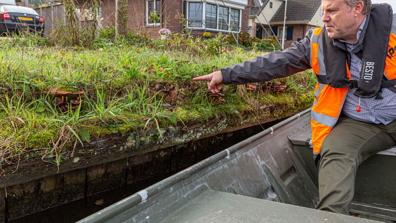 Medewerker wijst vanaf boot naar oever tijdens inspectie van watergang in woonwijk, onderdeel van onderhoudswerkzaamheden