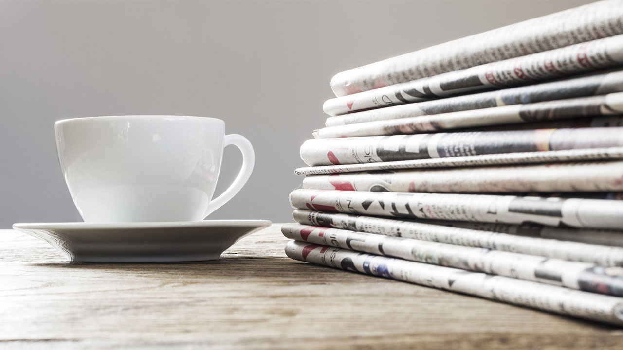 Een kopje koffie op een tafel naast een stapel kranten