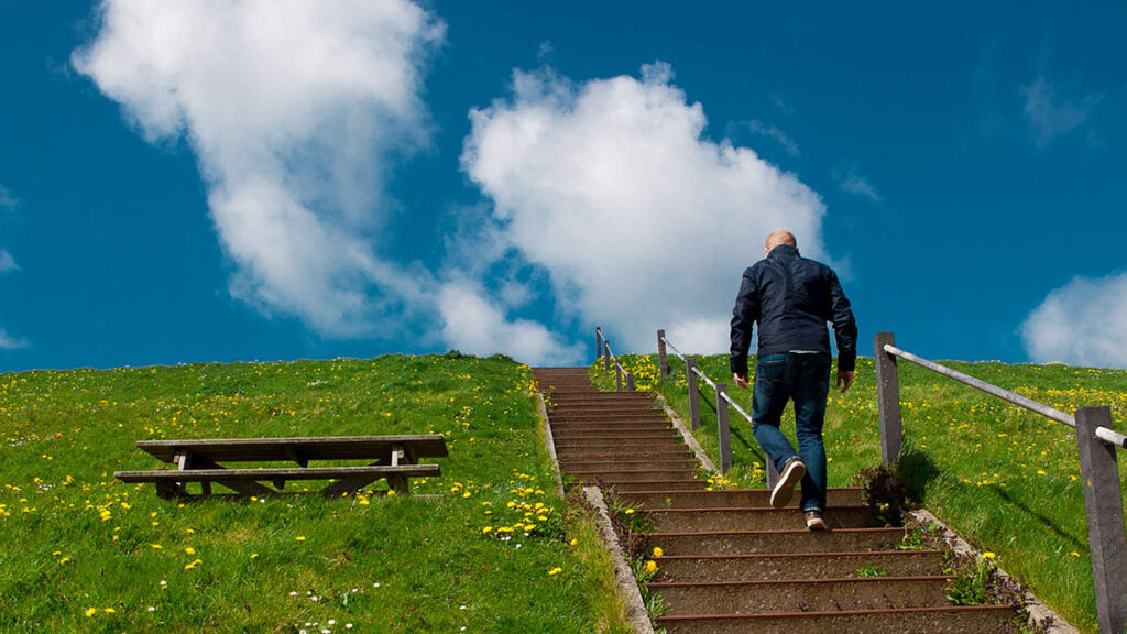Man in donker jasje beklimt betonnen trap naast grasheuvel