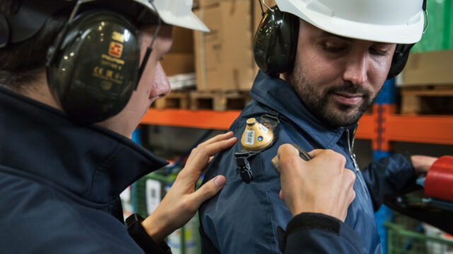 Arbeidshygiënist plaatst geluidsmeetapparatuur op schouder van medewerker voor meting blootstelling geluid