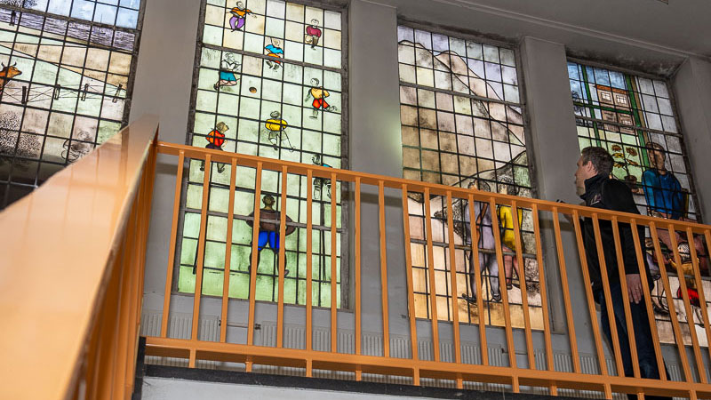 Man staat bij glas in loop bovenaan trap