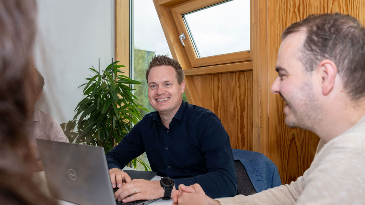 Overleg aan tafel met laptop en planten, illustratie van samenwerking en strategie in toekomstgericht vastgoedmanagement