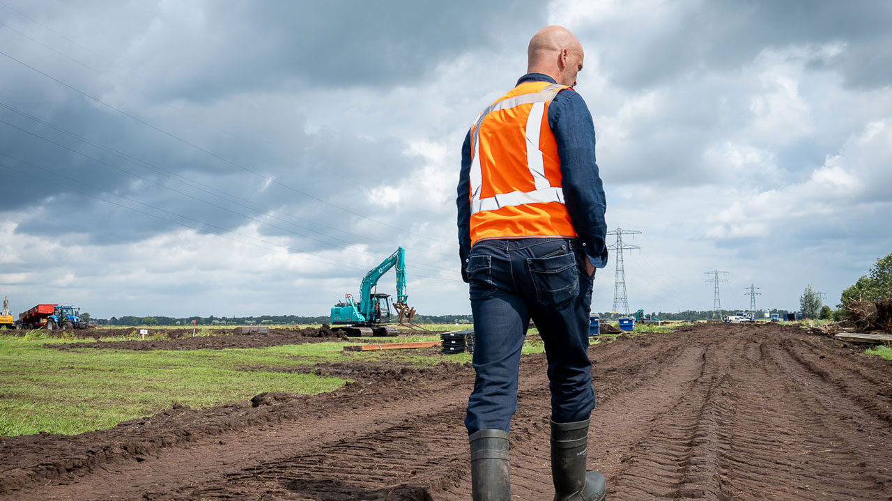 Medewerker loopt over zandpad in veenweidegebied Krimpenerwaard waar gewerkt wordt aan 2.250 hectare nieuwe natuur en waterbeheer