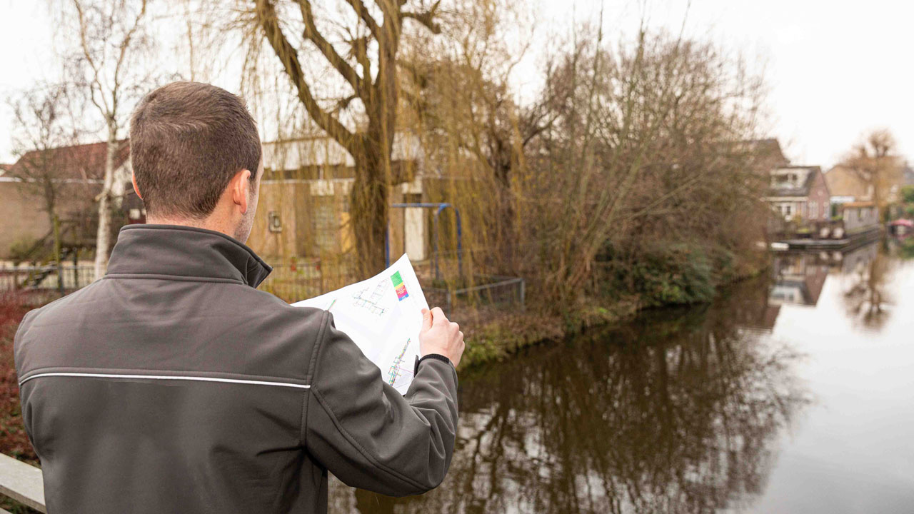Medewerker bij water met sloopdocument, betrokken bij circulaire sloop van schoolgebouw Sterrenwerk in Teylingen