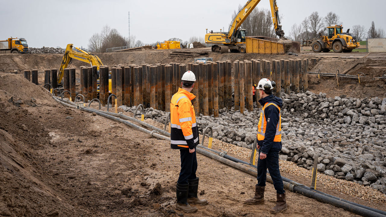 Bouwplaats met dijkversterking, zwaar materieel en inspecterende medewerkers – onderdeel van project De Dijk van de Toekomst