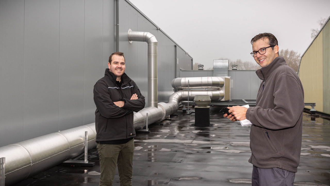 Adviseurs inspecteren installaties op industrieel dak in kader van energieprestatie volgens NTA 8800, met tablet en ventilatiesystemen