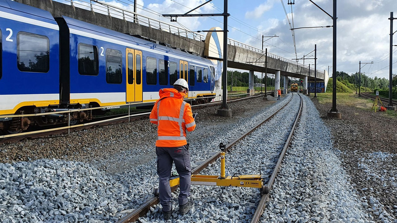Spoorwerker meet rails voor passerende trein, illustratie van digitalisering en onderhoud van spoorinfrastructuur binnen GRIP-samenwerking