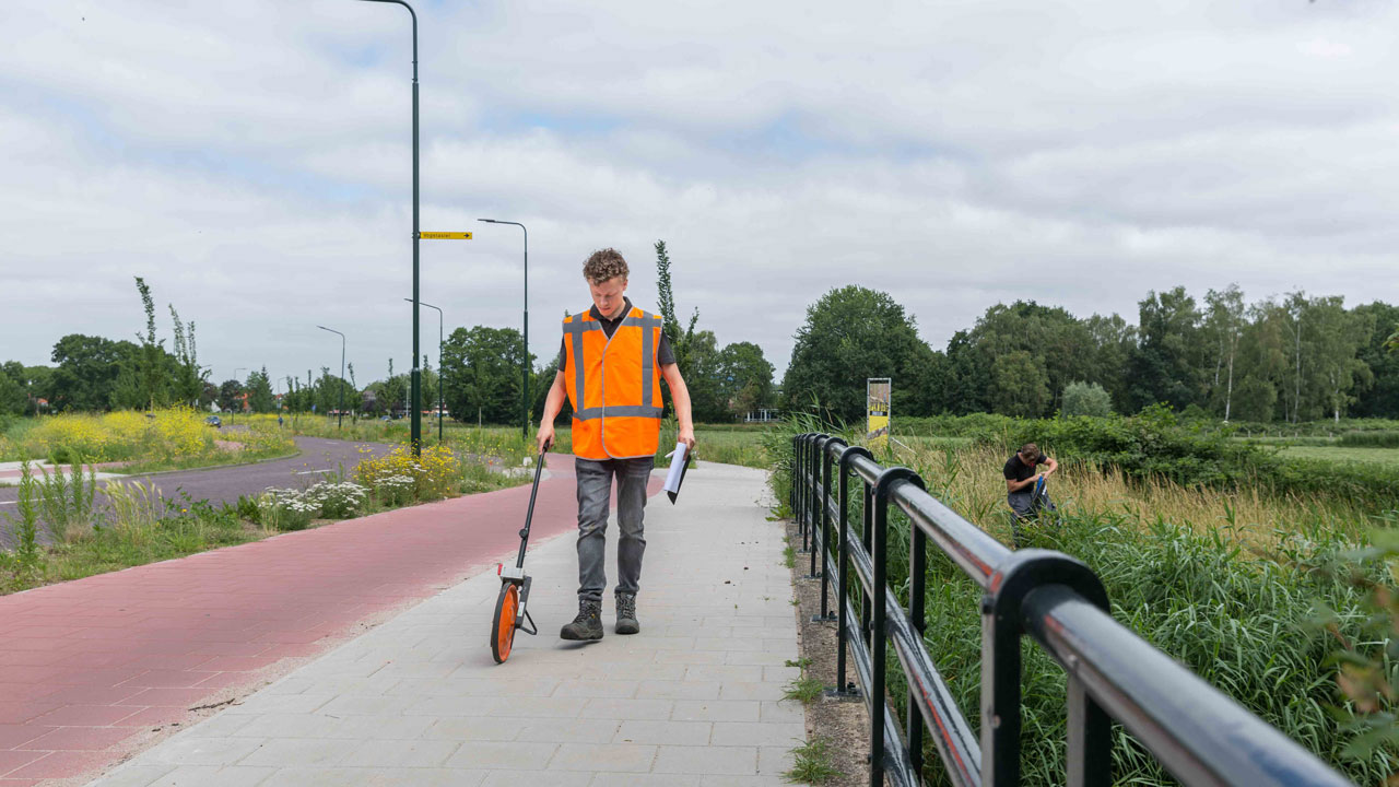 Inspecteur met meetwiel op fietspad in Gooise Meren tijdens kunstwerkinspectie, omgeven door groen en infrastructuur