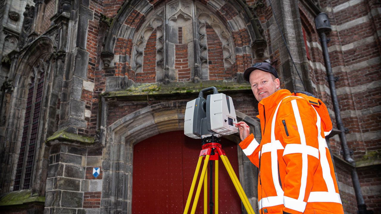 Landmeter met meetapparatuur voor de Oude Kerk Amsterdam, bezig met 3D-opname van historische gevels en bouwkundige details