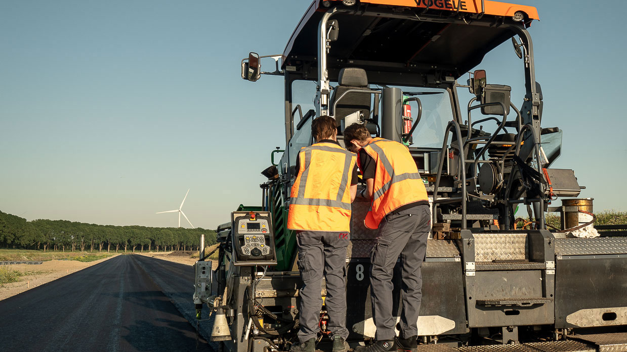 Medewerkers voeren metingen voor asfaltrook uit tijdens wegwerkzaamheden op asfalteermachine