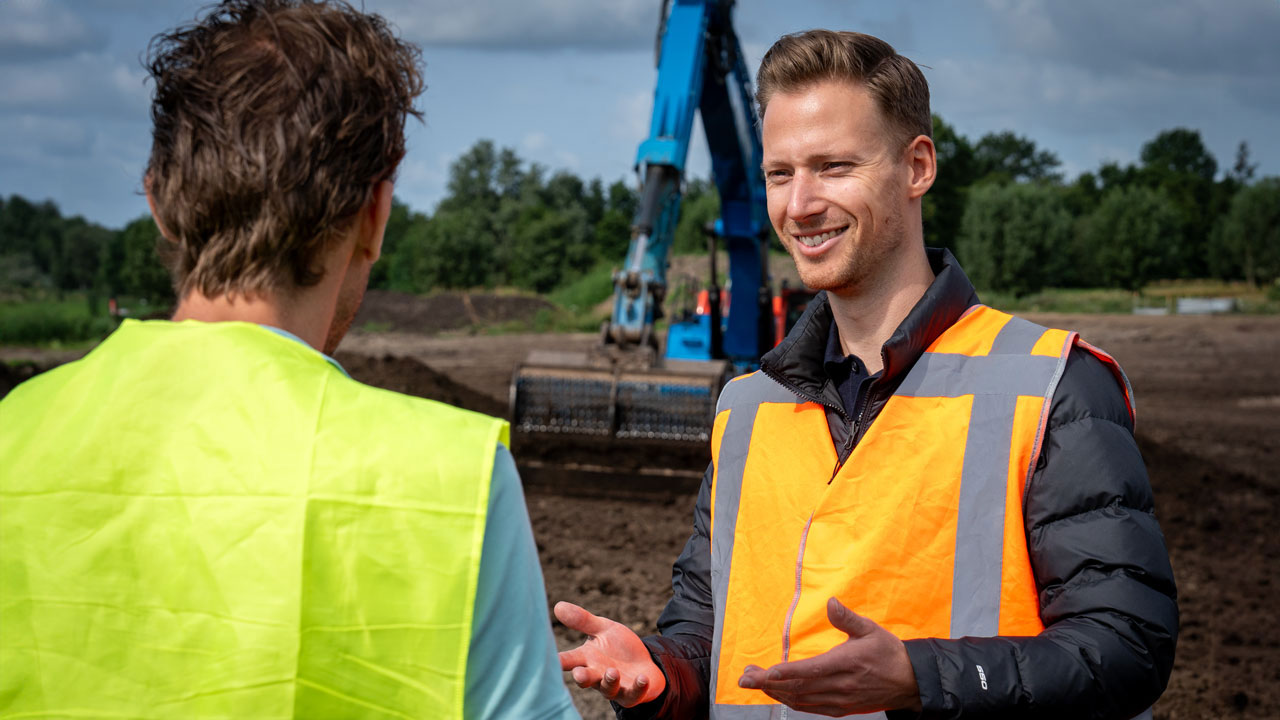 Twee personen in veiligheidsvesten overleggen op een bouwlocatie