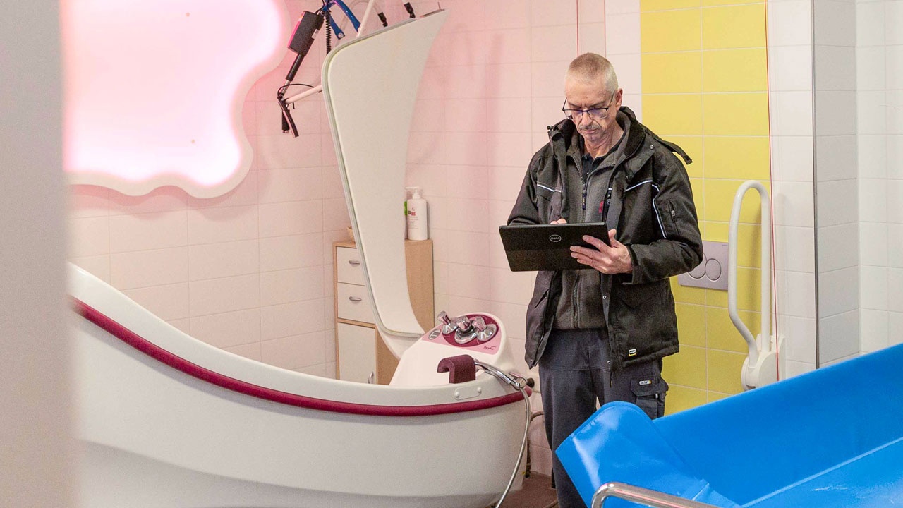 Inspecteur met tablet in sanitaire ruimte Amarant met bad, tillift en inspectieapparatuur voor legionellapreventie