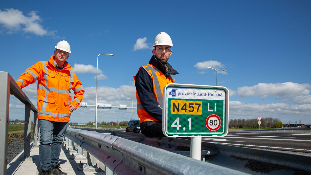 Twee arbeiders staan ​​naast een verkeersbord N457 op een brugviaduct