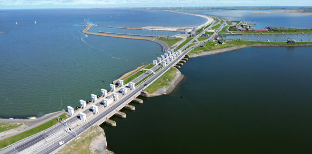 Luchtfoto van waterkering met sluizen en wegen, illustratief voor infrastructuurprojecten in waterbeheer en ruimtelijke ordening