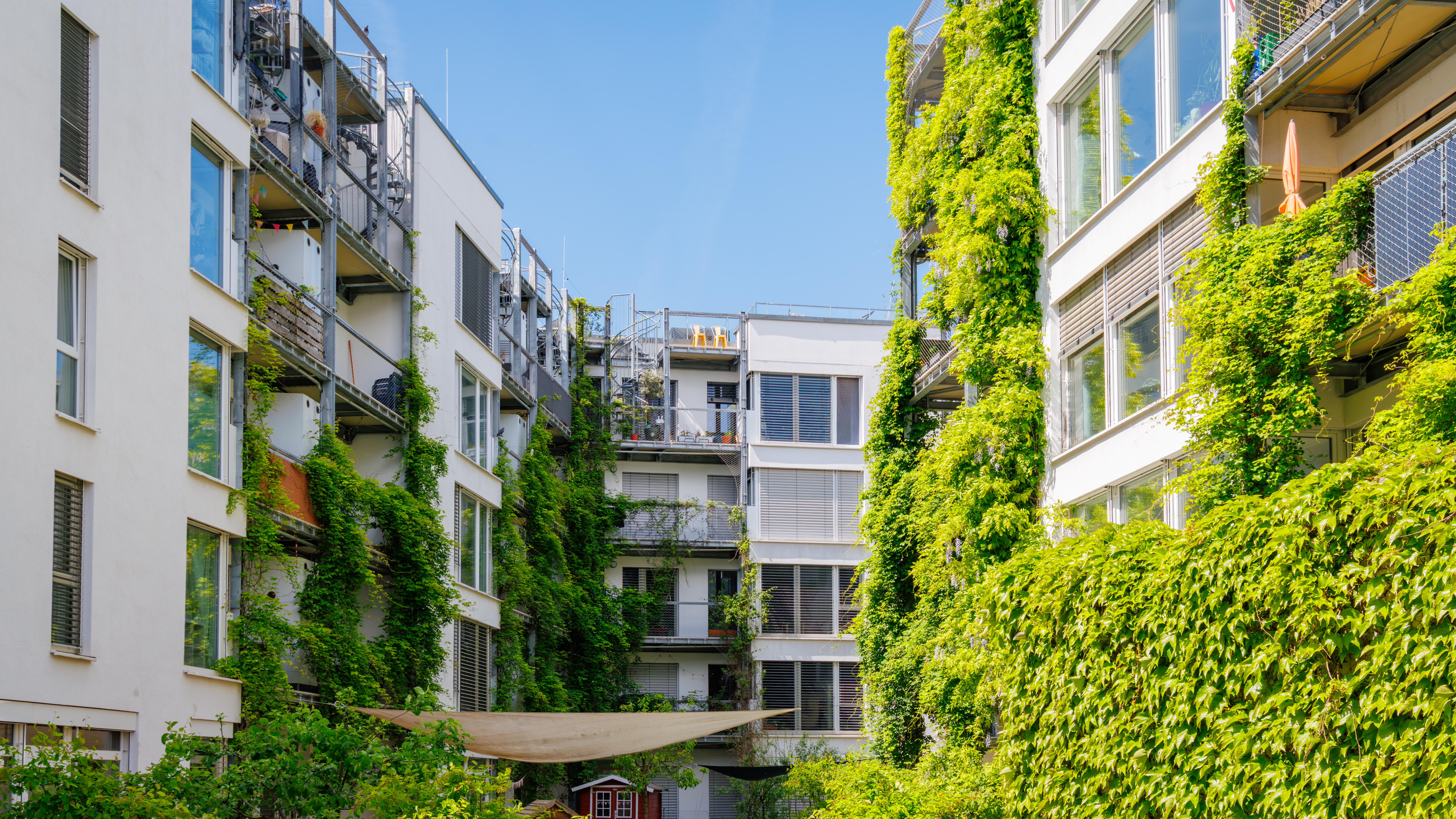 Moderne gebouwen met glazen gevels en geïntegreerd groen, illustratief voor gezonde en comfortabele werkomgevingen volgens WELL