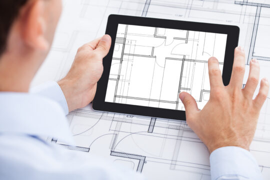 Man met tablet en bouwtekeningen, visualisatie van digitaal tekeningenbeheer en informatiemanagement in de bouwsector