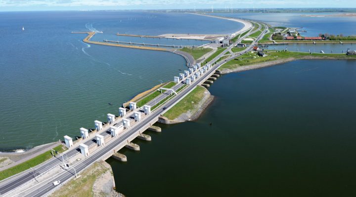 Luchtfoto van waterkering met sluizen en wegen, illustratief voor infrastructuurprojecten in waterbeheer en ruimtelijke ordening