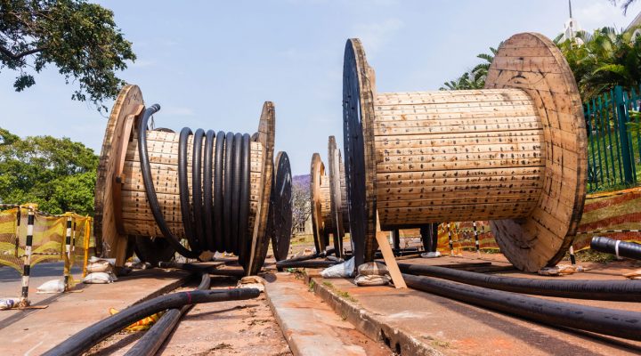 Grote houten kabelhaspels met uitgerolde kabels op verhard terrein, illustratief voor aanleg en verlegging van ondergrondse infrastructuur