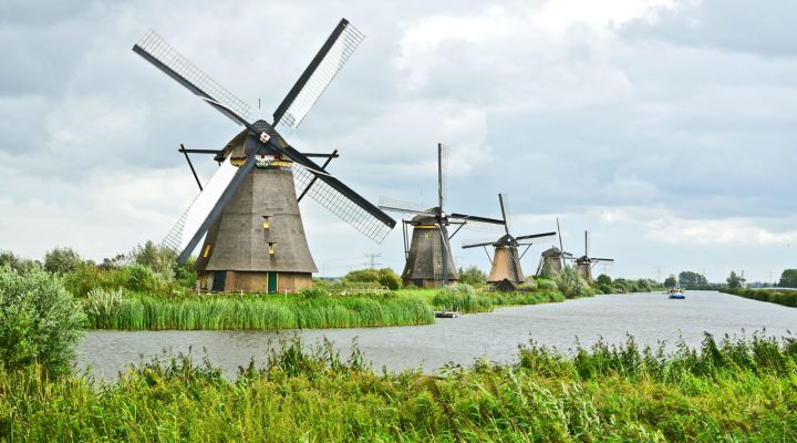 Traditionele Nederlandse windmolens langs een watergang, met groene oevers op de voorgrond en een bewolkte lucht erboven — symbool voor het samenspel tussen waterbeheer en bodemkwaliteit