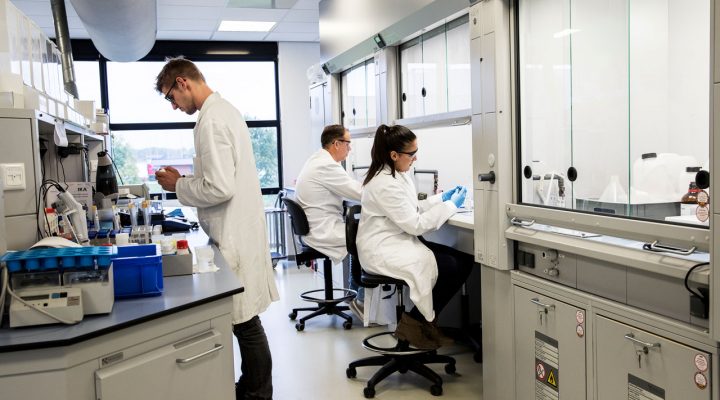 Laboratoriummedewerkers voeren chemische analyses uit onder afzuigkasten in een goed uitgeruste onderzoeksruimte