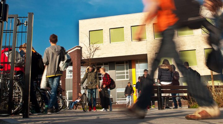 Schoolgebouw met grote ramen en leerlingen buiten op het plein; zonnige dag, levendige sfeer, gericht op beheer en onderhoud van scholen